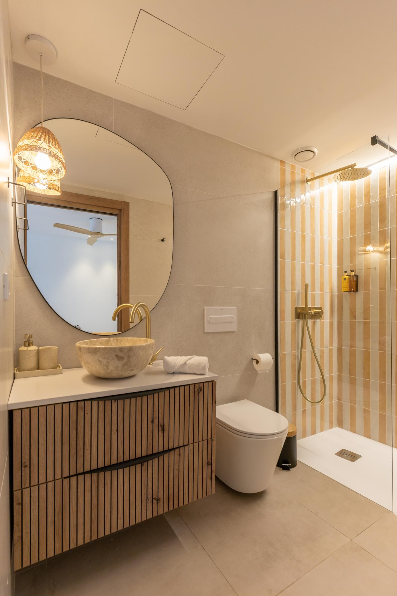 Een moderne badkamer met een ronde spiegel, een wastafel op voet, toilet en een inloopdouche.