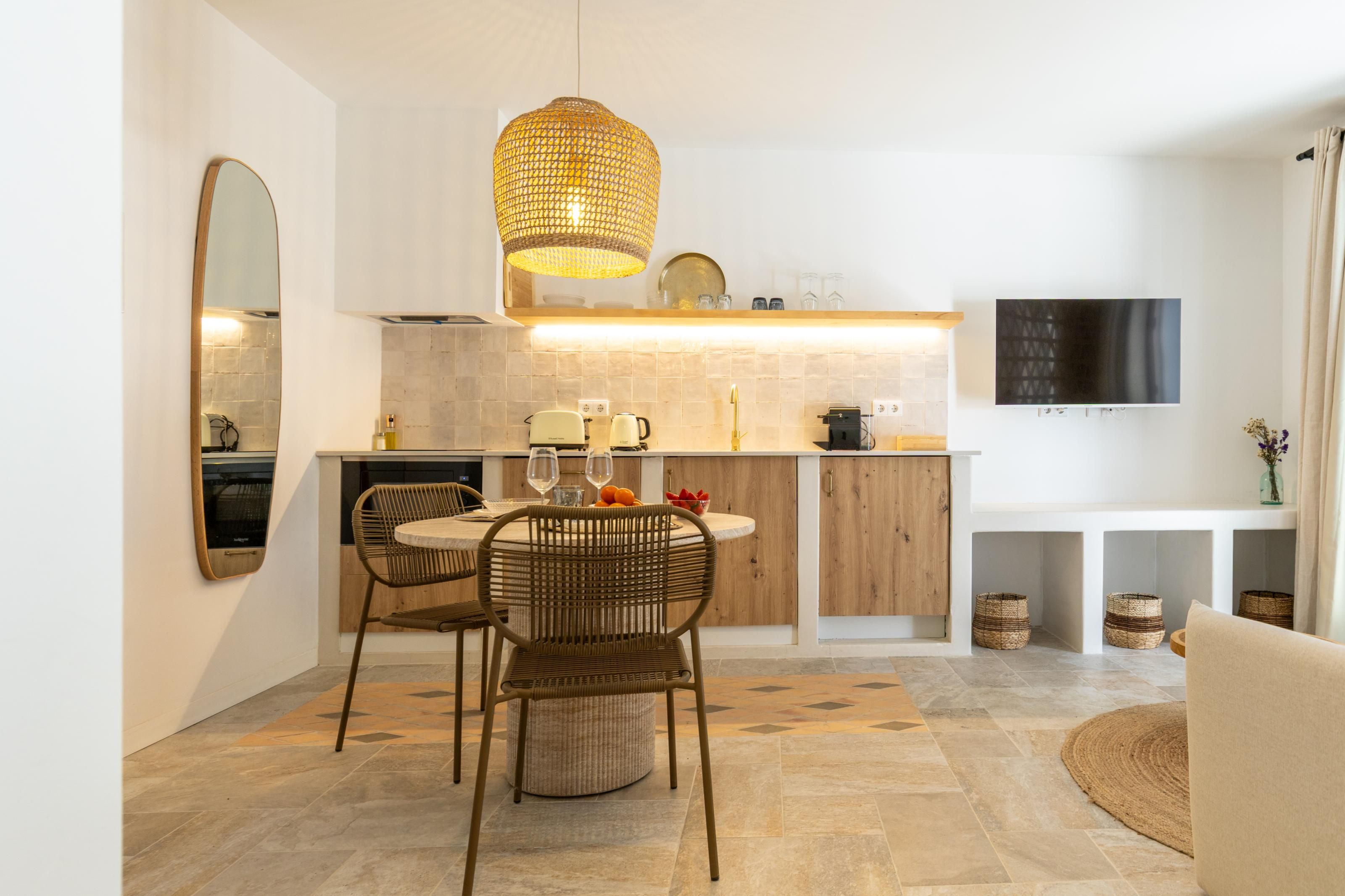 Cozinha moderna com área de refeições, destacando uma mesa redonda, cadeiras de vime e um lustre.