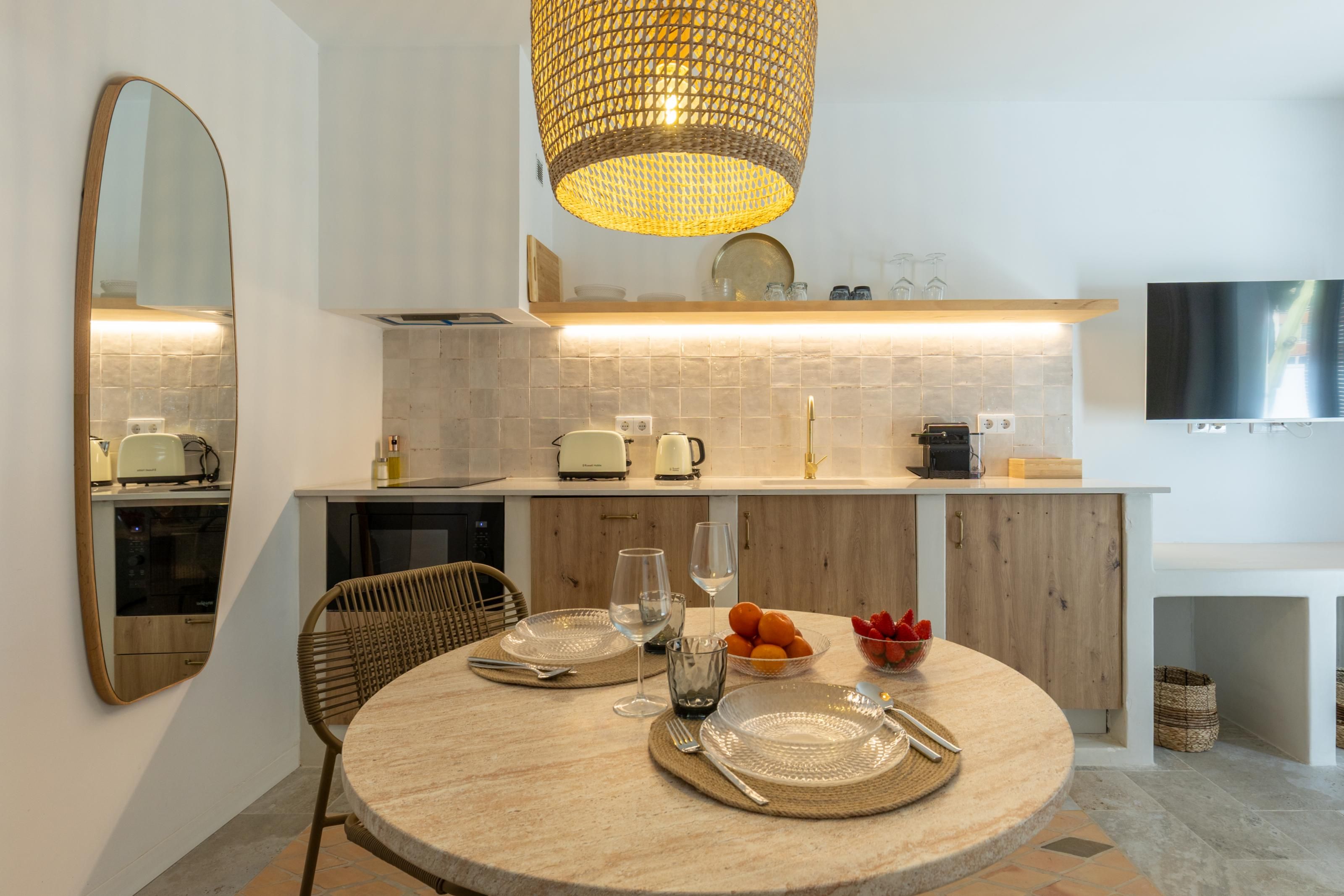 Een moderne keuken met een ronde eettafel, een hanglamp en een flatscreen televisie aan de muur.