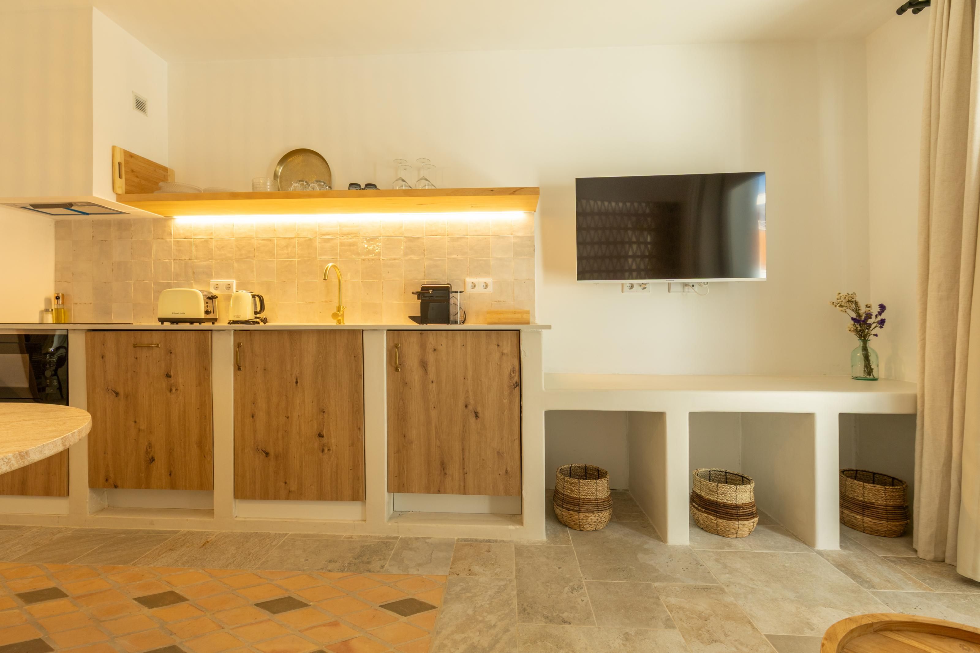 Une cuisine moderne avec des meubles en bois, un four encastré et un téléviseur à écran plat fixé au mur.