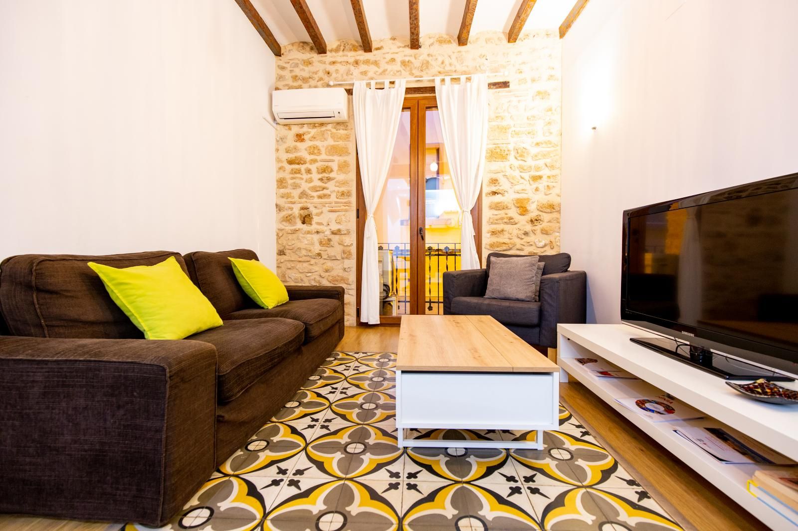 Un salon chaleureux avec un canapé marron, une table basse blanche et un téléviseur à écran plat posé sur un meuble blanc.