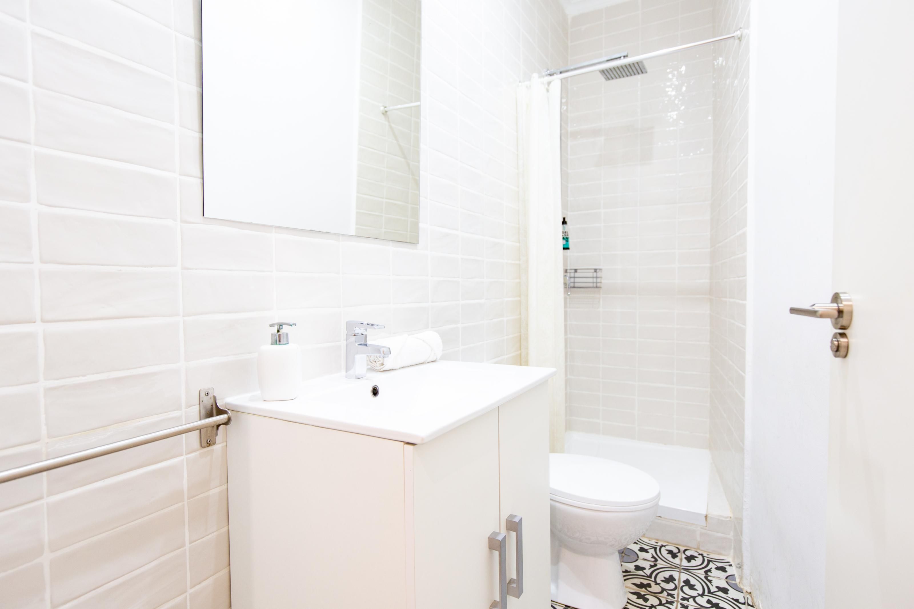 Une salle de bain moderne avec des carreaux blancs, des toilettes, un lavabo avec un miroir et un espace douche.