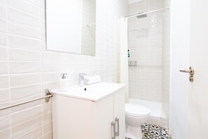 Une salle de bain moderne avec des carreaux blancs, des toilettes, un lavabo avec un miroir et un espace douche.