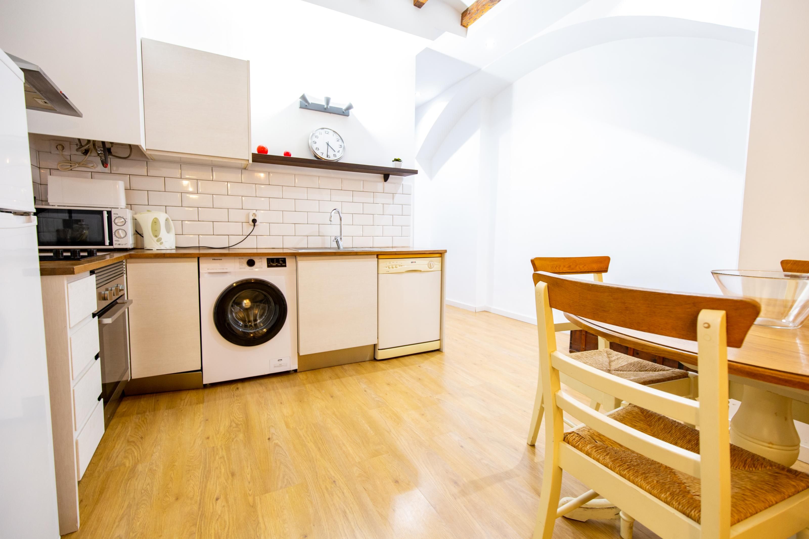 Une cuisine de taille réduite équipée d’un lave-linge, d’un four à micro-ondes et d’une horloge murale.
