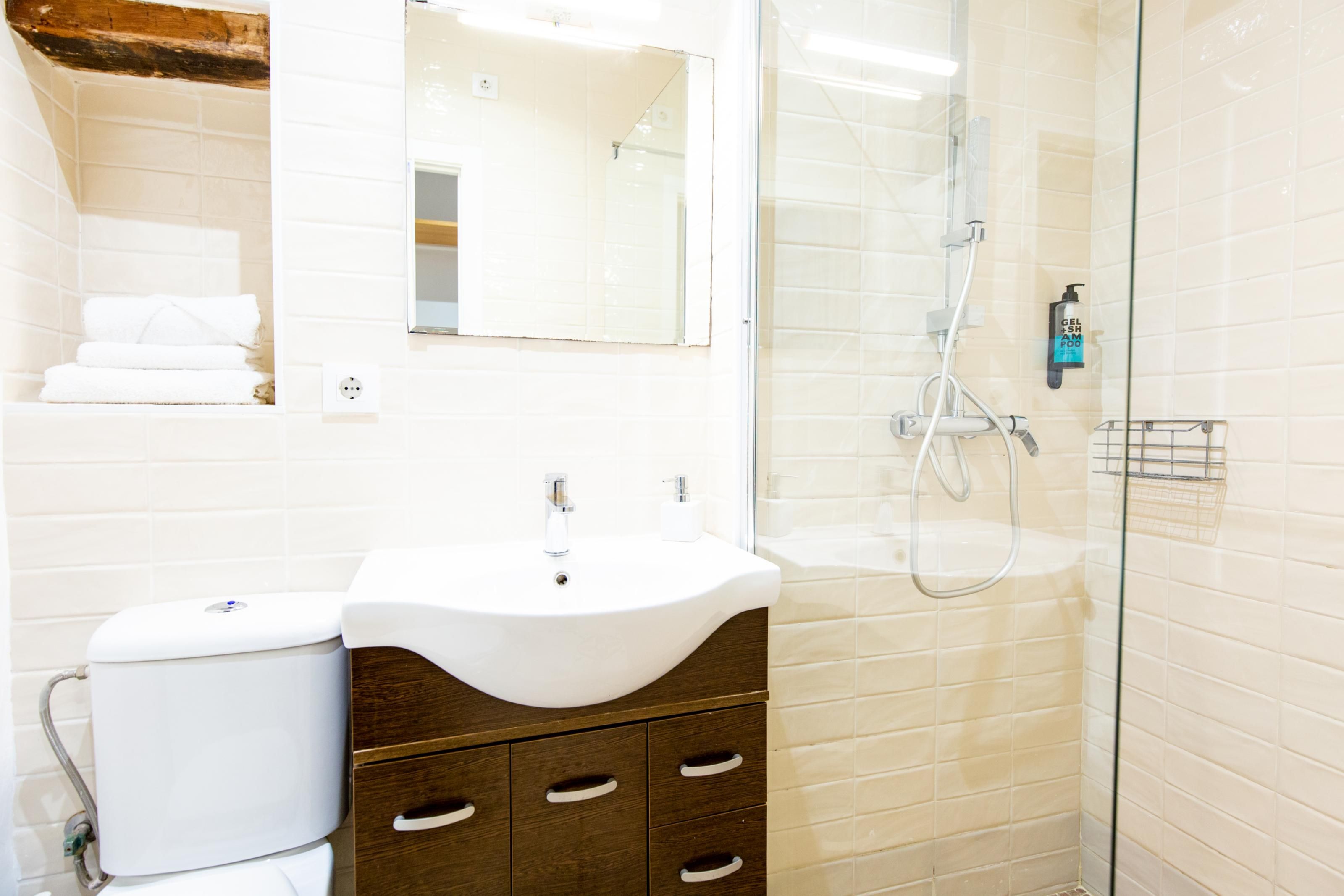 A modern bathroom with a white sink, a mirror, a glass shower enclosure, and a towel rack.