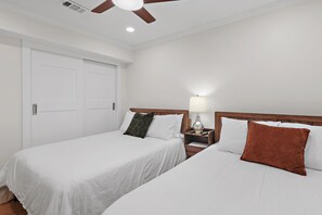 Une chambre d’hôtel avec deux lits, un ventilateur de plafond, une table de chevet avec une lampe et une porte.
