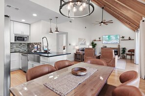 Eine moderne Küche mit Mikrowelle, ein Essbereich mit Holztisch und Ledersesseln sowie ein Wohnbereich mit Kamin und Fernseher.