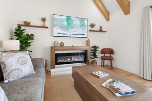 Ein Wohnzimmer mit Kamin, einem an der Wand befestigten Fernseher, einem Holztisch und einer Couch mit dekorativen Kissen.