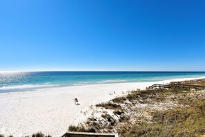 Ein Strand mit einem hölzernen Promenadenweg zum Wasser, klarem Himmel und einem sandigen Ufer.