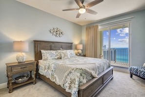A bedroom with a large bed, a ceiling fan, a nightstand with a lamp, a decorative wall piece, and a view of the ocean through a balcony. - ⛱️ Walk to Beach~19th floor Gulf Views~2 Pools~The Radiant Vista☀️ (Miramar Beach)