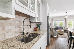 Une cuisine dotée de plans de travail en granit, d’éviers en acier inoxydable et de meubles blancs.