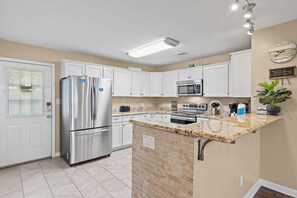 Una cocina moderna con armarios blancos, electrodomésticos de acero inoxidable, encimera de granito y un reloj en la pared.