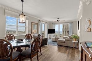 A spacious living room with a dining area, a ceiling fan, and a large window with a view. - Gulf Views⛱️Walk to Beach-Kids Fountain~2 Pools-Ariel Dunes I 801-Morning Raes☀️ (Miramar Beach)