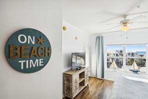 Ein Zimmer mit großem Fenster, Deckenventilator, Holzschrank und einer Wandtafel mit der Aufschrift 'ON BEACH TIME'.
