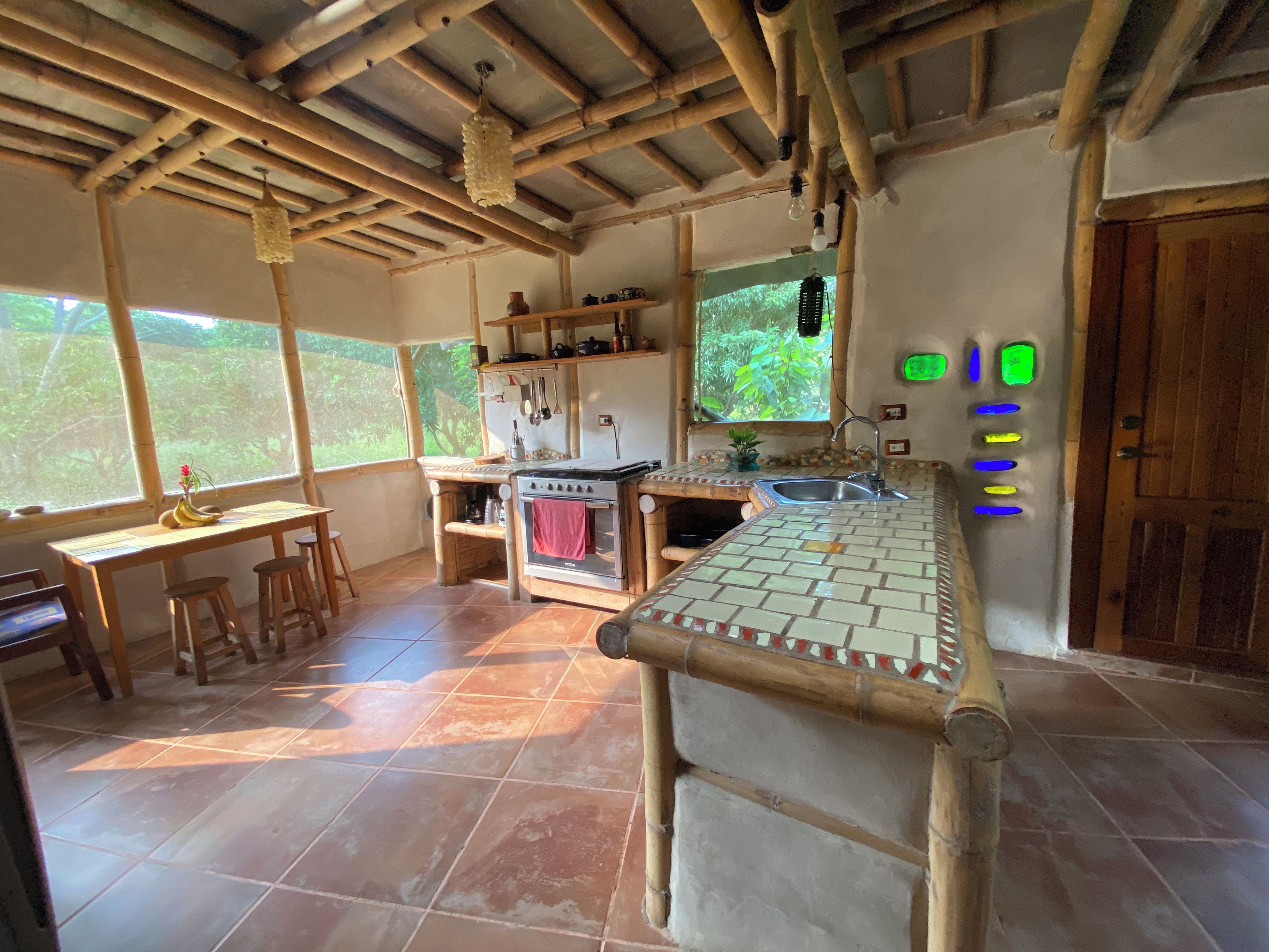 Uma cozinha rústica com teto de madeira, fogão, pia e janela com vista para o verde.