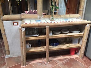 A bamboo shelf unit with storage shelves, a white refrigerator, and a tiled floor.