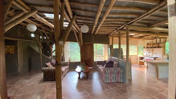 Interior rústico com teto de bambu, um sofá, uma mesa pequena e uma área de cozinha.