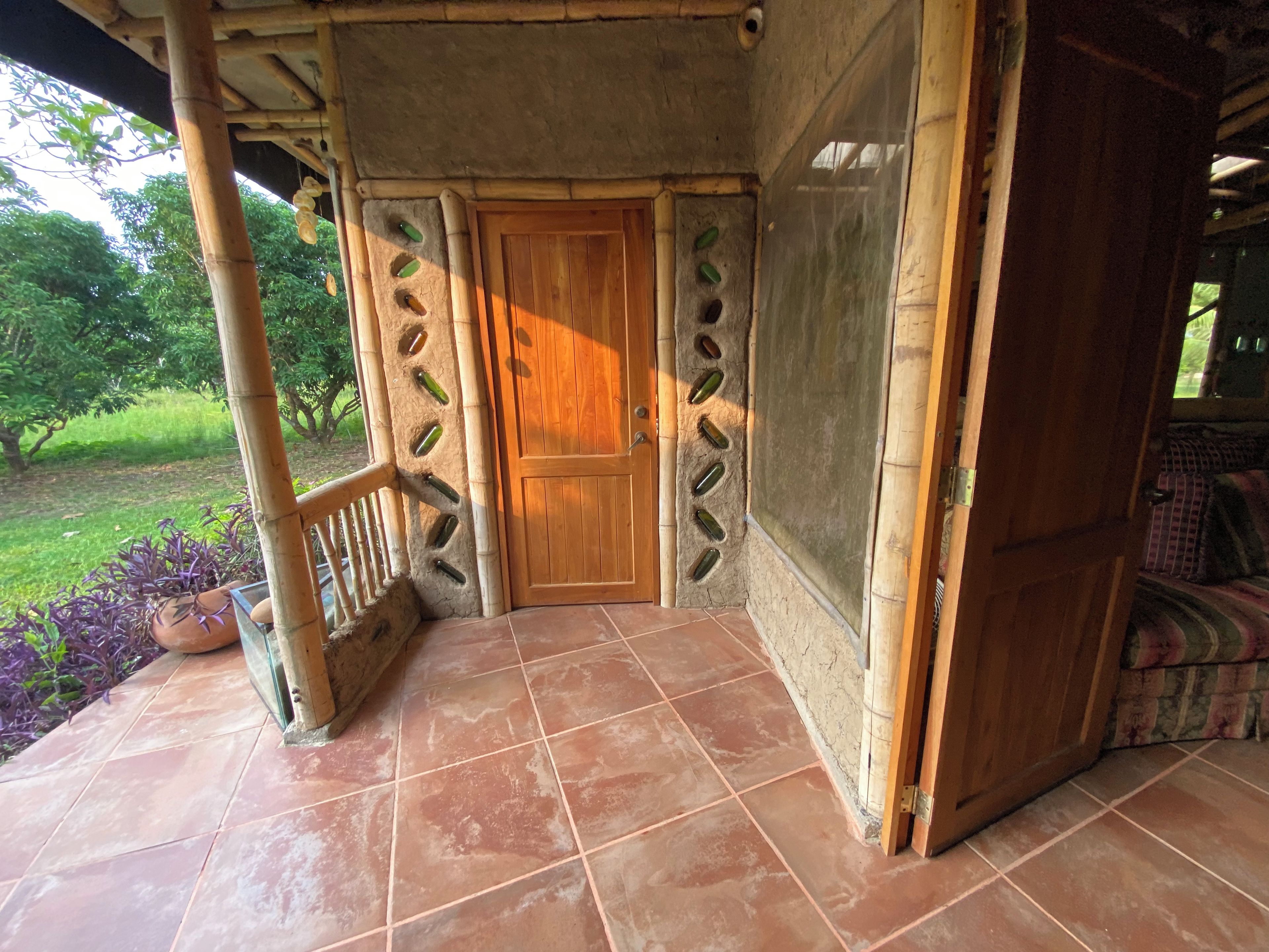 Una puerta de madera con mosquitera, piso de baldosas y barandilla.