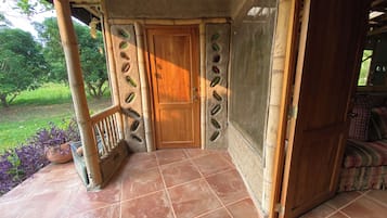 Una puerta de madera con mosquitera, piso de baldosas y barandilla.