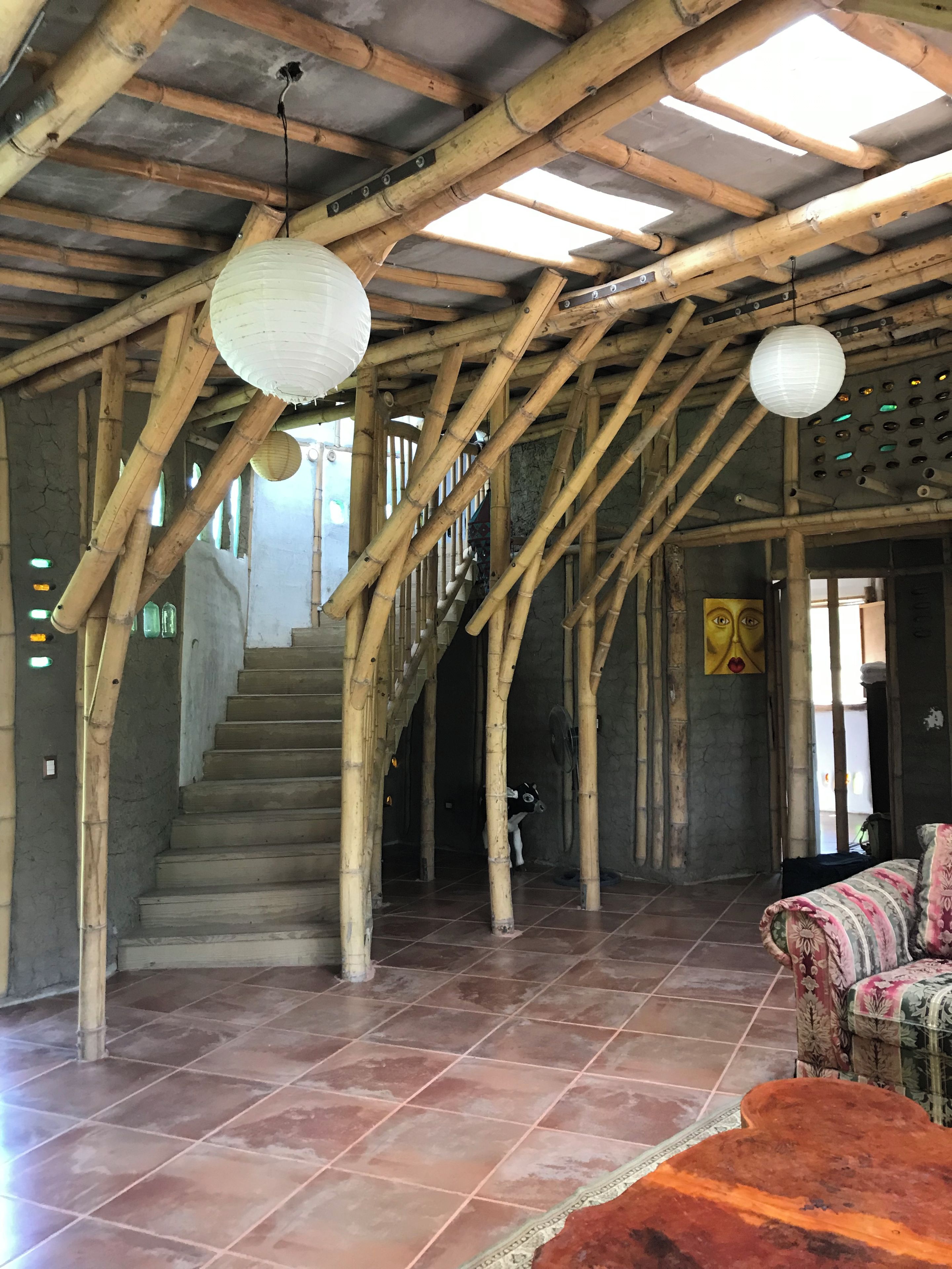 A staircase with bamboo beams, a fan, and a patterned sofa in a rustic interior.