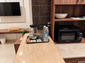 A kitchen with a microwave, a coffee maker, a kettle, and a tray with food items and water bottles. - Bohohomes sea view (Red Sea Governorate)