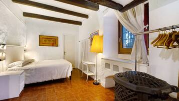 Une chambre à coucher comprenant un lit, une table de chevet, une lampe, un radiateur, une fenêtre avec des rideaux et un porte-manteau.