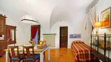 Una habitación con una mesa de comedor, sillas, una cama con colcha a cuadros, un radiador, una lámpara de pared y un cuadro enmarcado.