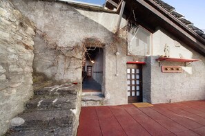 Un edificio de piedra con una escalera de madera roja que lleva a una puerta, una ventana pequeña y un toldo rojo.