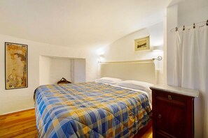 Un dormitorio con cama, suelo de madera, cabecera, mesita de noche, lámpara de pared y un cuadro.