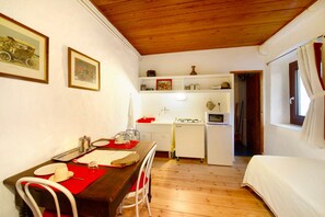 Una habitación compacta con techo de madera, una mesa de comedor con sillas, una cama, kitchenette y una puerta que da a otra habitación.