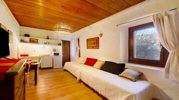 Ett mysigt rum med ett träpanelat tak, en soffa med kuddar, ett matbord med stolar, en köksdel och ett fönster med gardiner.