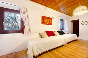 A room with wooden flooring, a bed with a white bedspread, two windows with curtains, and a wooden ceiling.