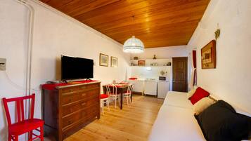 Una habitación acogedora con techo de madera, un televisor sobre un aparador, una mesa de comedor con sillas y un sofá con cojines.