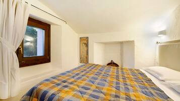 Une chambre avec une couvre-lit à carreaux, une fenêtre avec des rideaux, une tête de lit en bois et un tableau accroché au mur.