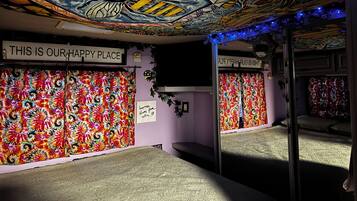 Una habitación con un tapiz floral vibrante y multicolores en las paredes, un techo con un mural detallado y un letrero que dice 'THIS IS OUR HAPPY PLACE'.