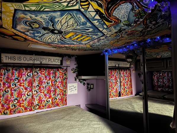 A room with a vibrant, multicolored floral tapestry on the walls, a ceiling with a detailed mural, and a sign that reads 'THIS IS OUR HAPPY PLACE.'