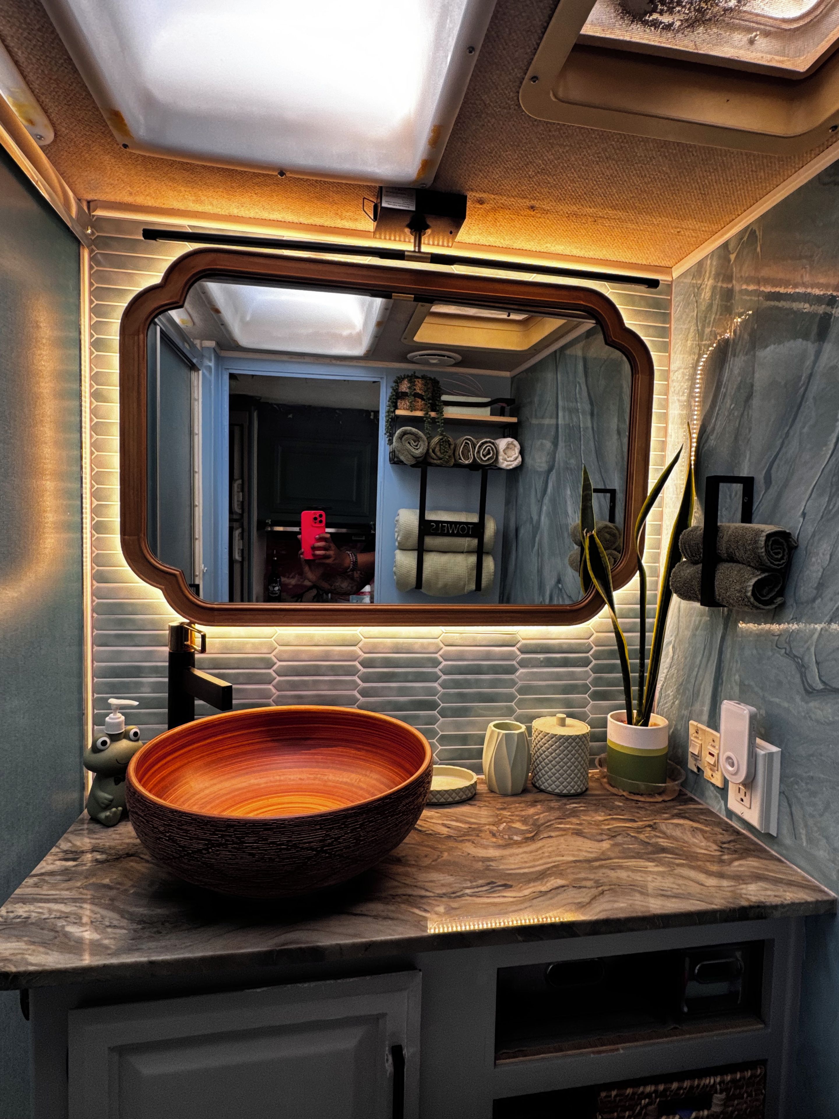 Un baño con un espejo grande, un lavabo redondo y un perchero con toallas.
