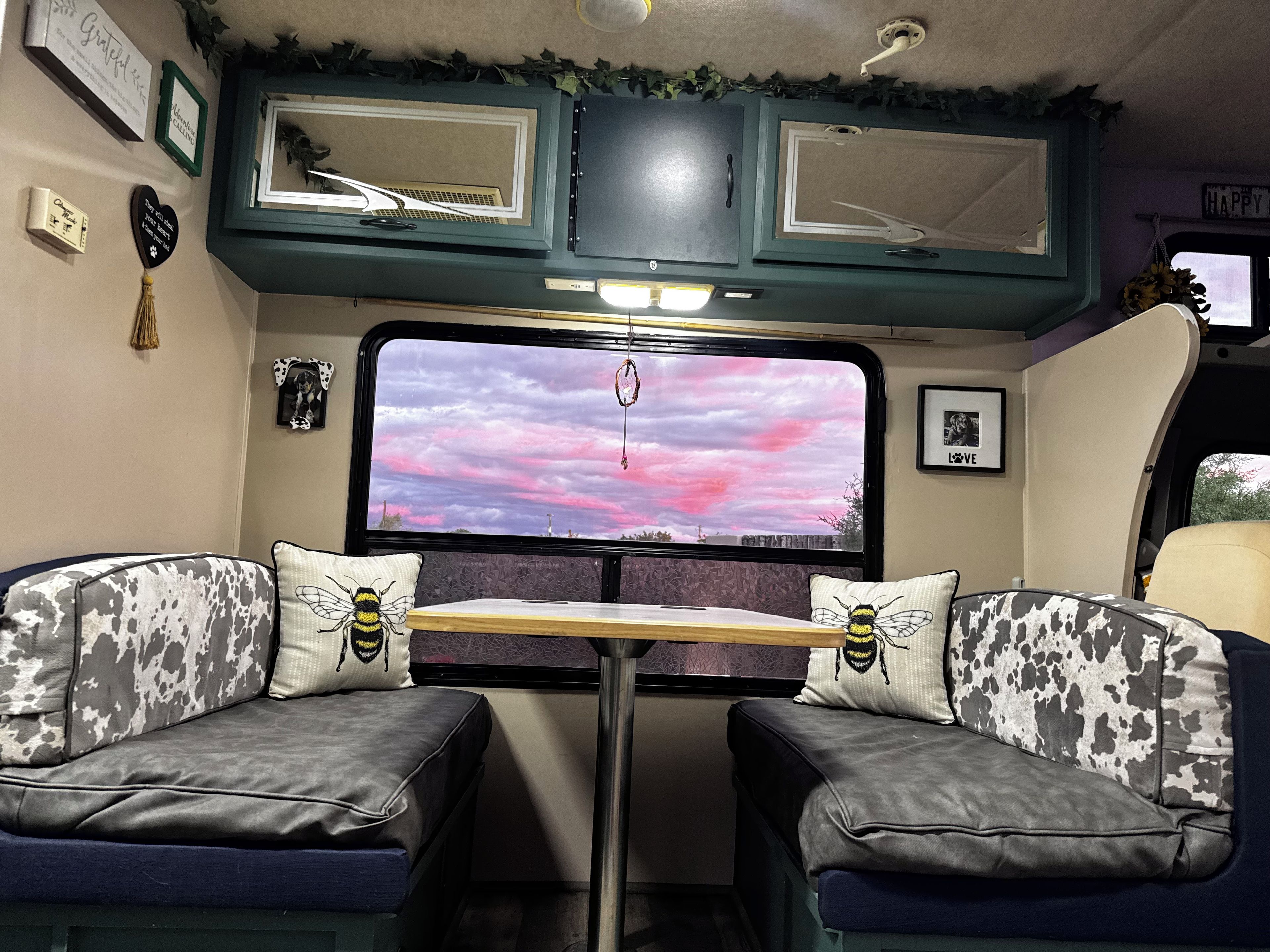 Un interior acogedor con una cama, una mesa y un amplio ventanal con vista a un cielo rosado.