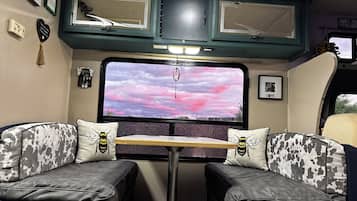 Un interior acogedor con una cama, una mesa y un amplio ventanal con vista a un cielo rosado.