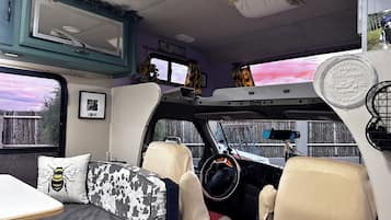 Interior de campervan con cama, zona de estar y volante.