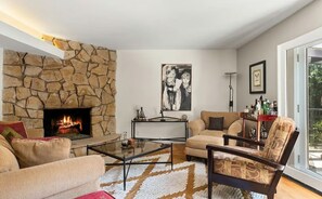 Ein Wohnzimmer mit Kamin aus Stein, einer Couch, einem Sessel und einem Couchtisch.