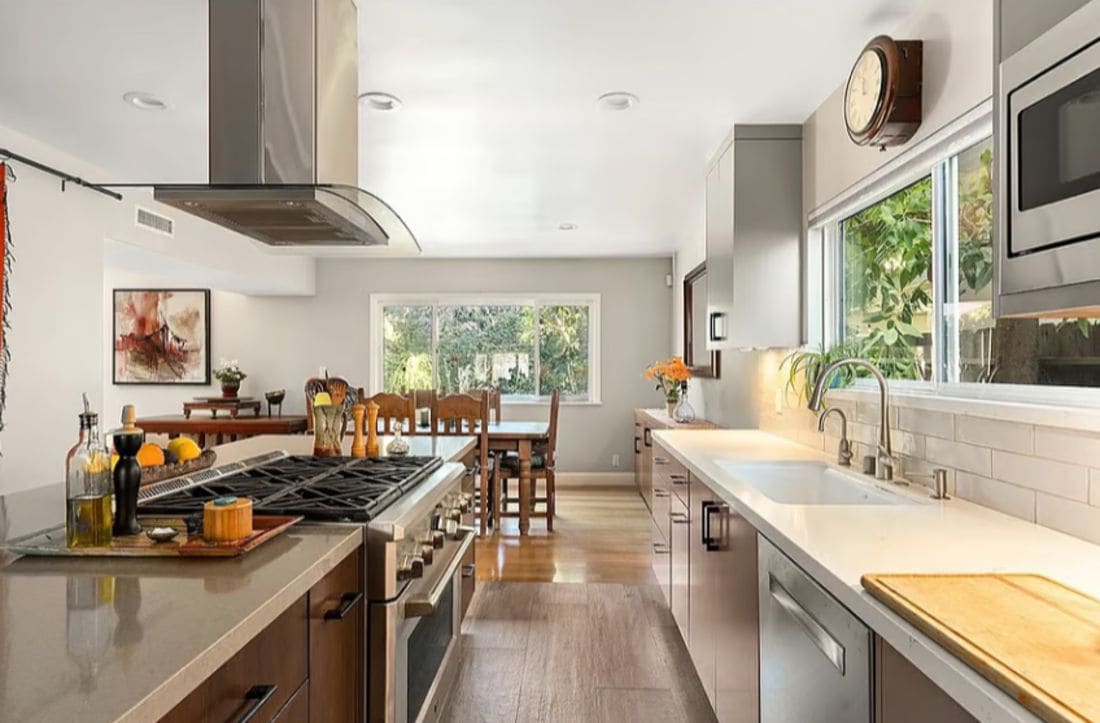 A modern kitchen with a gas stove, stainless steel appliances, and a large window providing natural light.