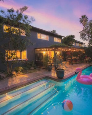 Ein Swimmingpool mit einem Flamingofloat und einem Strandball, umgeben von einer Terrasse mit Lichterketten.