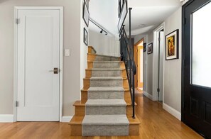 Eine Treppe mit Teppichstufen führt zu einer Zwischenebene, begleitet von Holzdielen und einem schwarzen Geländer.