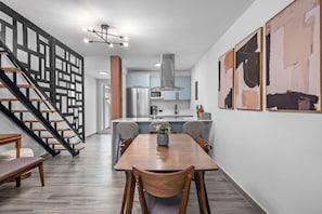 A modern kitchen with a central island, a dining area with a wooden table and chairs, and a staircase with a geometric railing. - Dorado Cove | Modern Pool & Beach Escape (Dorado)