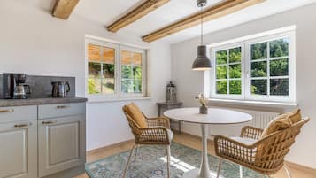 Eine moderne Küche mit Essbereich, inklusive eines runden Tisches, Korbstühle und Blick ins Grüne durch große Fenster.