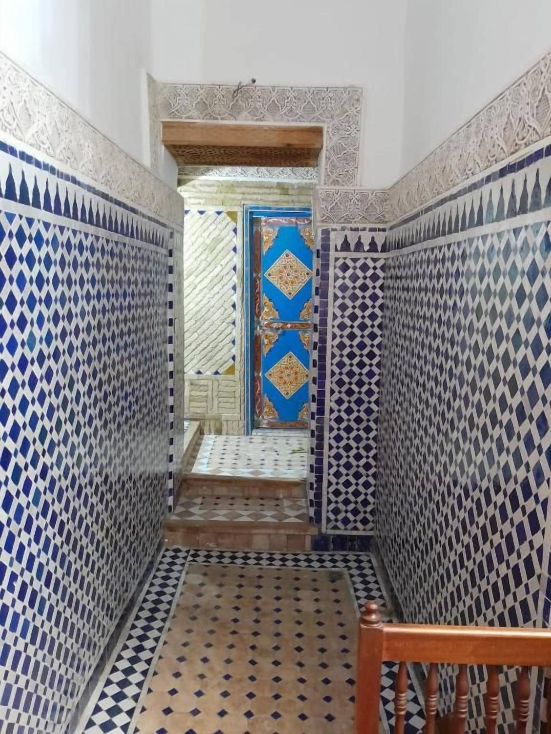 Un pasillo estrecho con paredes de baldosas estampadas y una silla de madera.