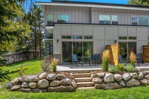 A modern two-story house with a patio, stone steps, and a wooden fence. - Charming Riverfront Property Close to the Resort! Pet Friendly! (Steamboat Springs)