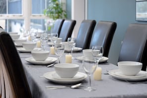 A dining table set with white bowls, plates, and wine glasses, with a candle on the table. - Finest Retreats | Westwell Hall (Ilfracombe)