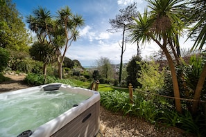 A hot tub surrounded by lush greenery and a view of a distant town. - Finest Retreats | Westwell Hall (Ilfracombe)